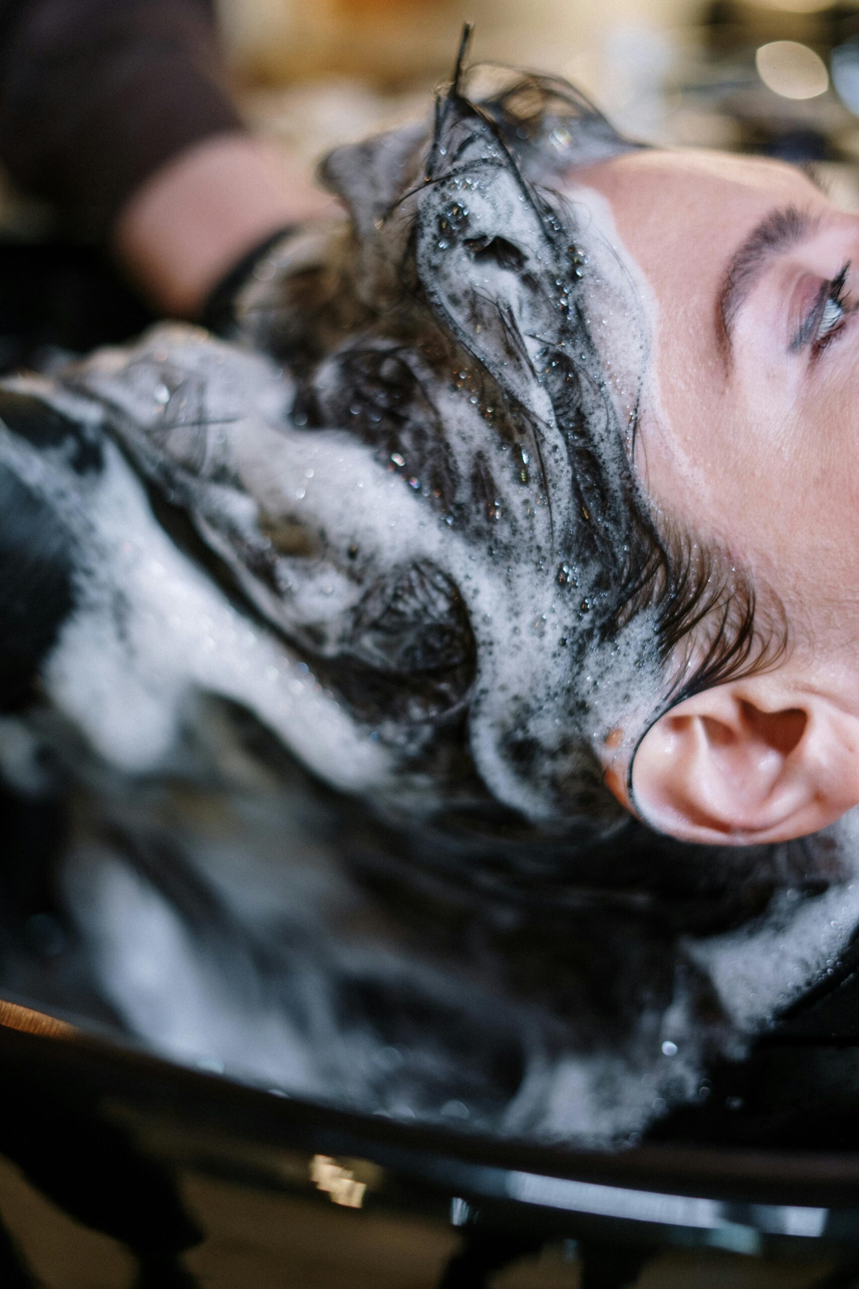 pexels-photo-3993454-3993454 Close-up of a woman getting her hair washed at a salon, covered in shampoo foam.
